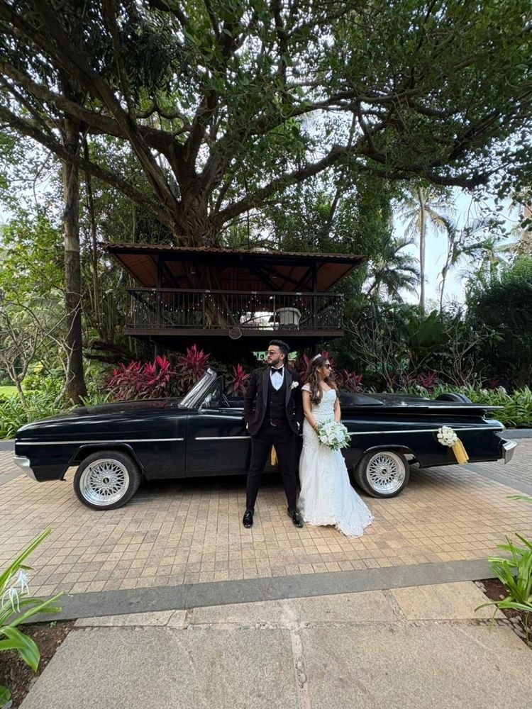 Couple standing by a black convertible under a banyan tree