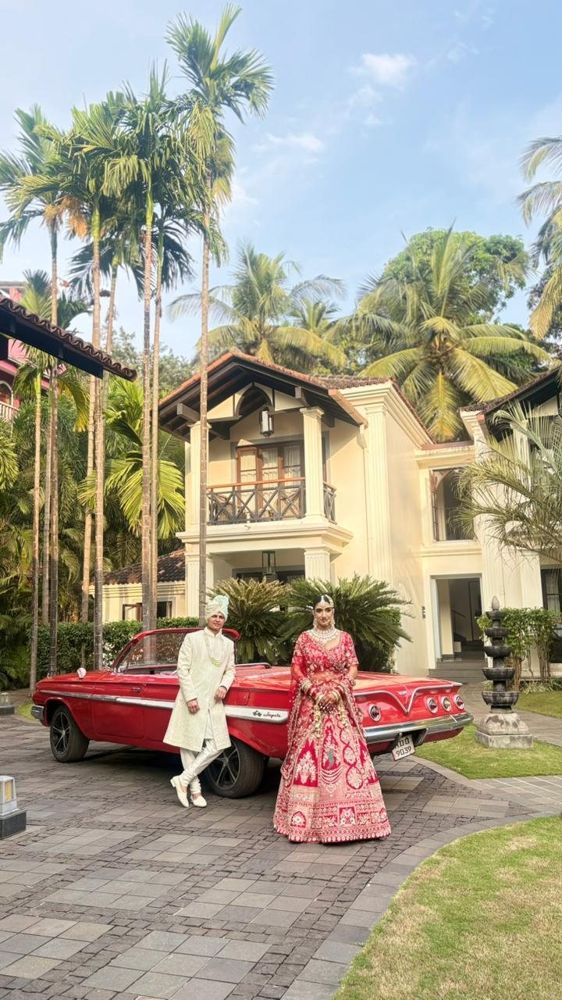 Bride and groom in traditional wear with the red Impala at a villa