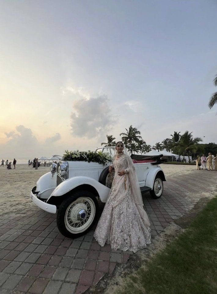 Bride in a lehenga beside the white vintage tourer on the beach at sunset