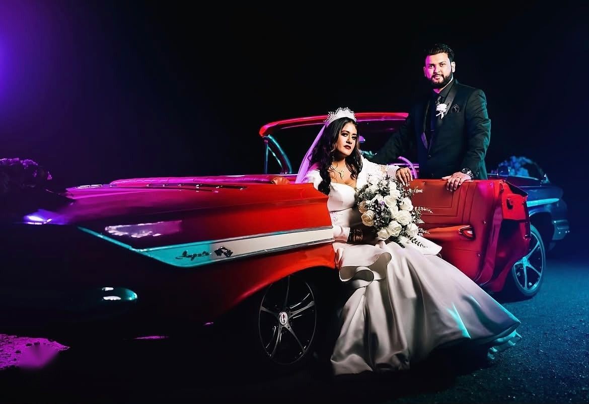 Bride and groom with a red Chevrolet Impala convertible under purple evening light
